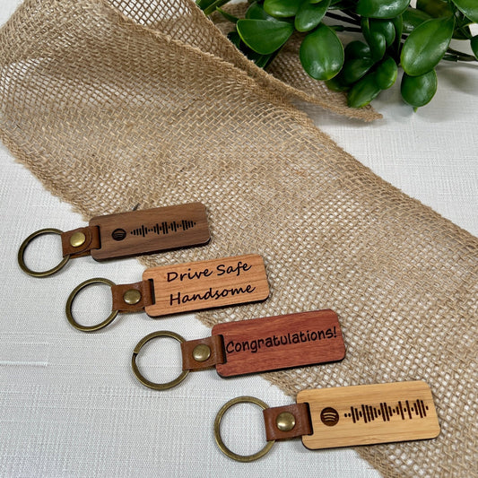 walnut, cherry, rosewood and bamboo engraved keychains. Image shows spotify engraved code, drive safe handsome and congratulations
